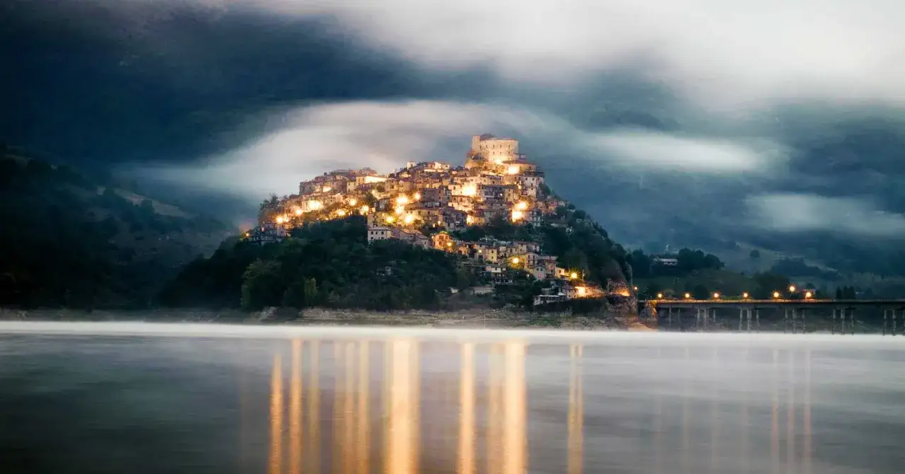 Borgo illuminato su una collina, riflessi sull'acqua. Un gioiello tra le top 10 cose da vedere nel Lazio.