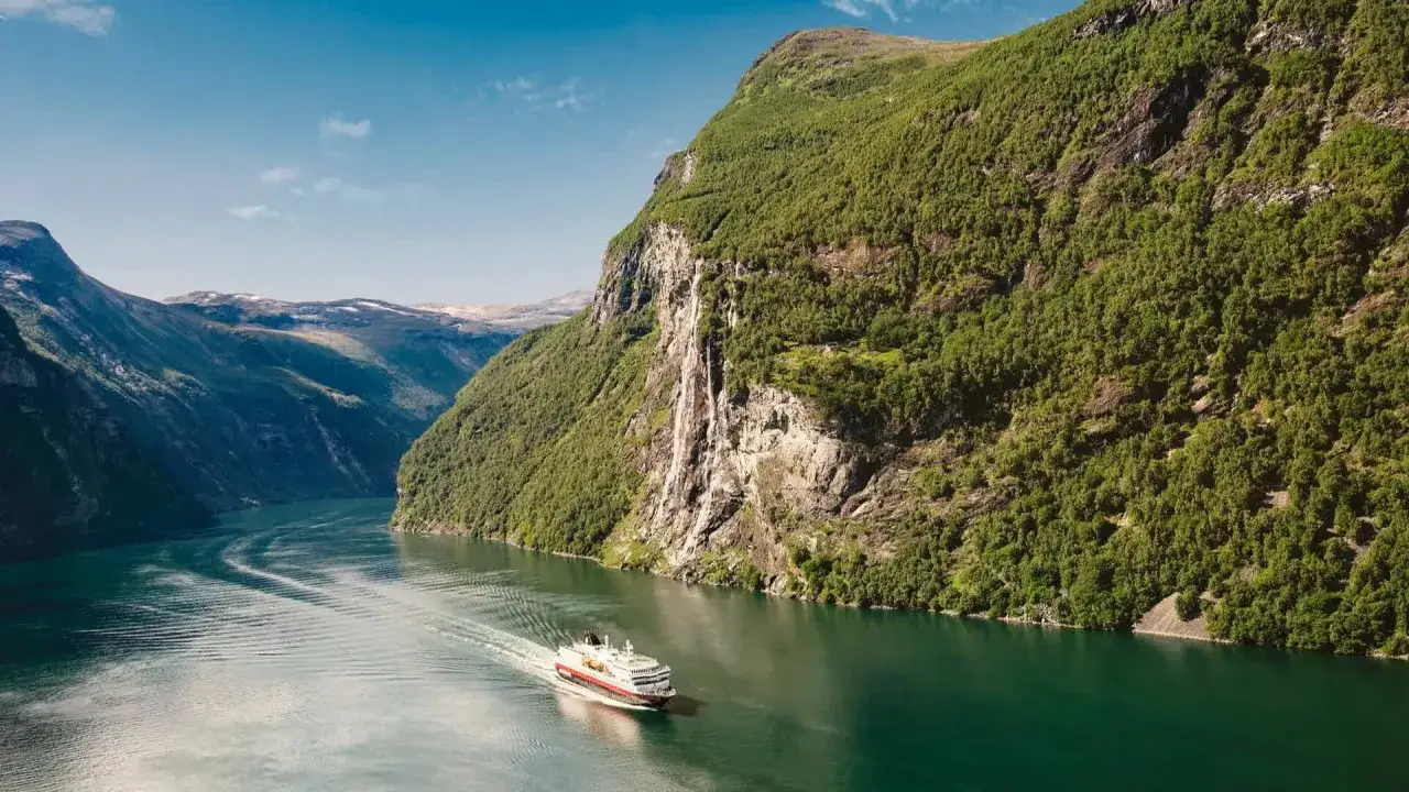 Nave in crociera tra fiordi norvegesi, con cascate e montagne verdi. Il periodo migliore per una crociera fiordi &egrave; l'estate.