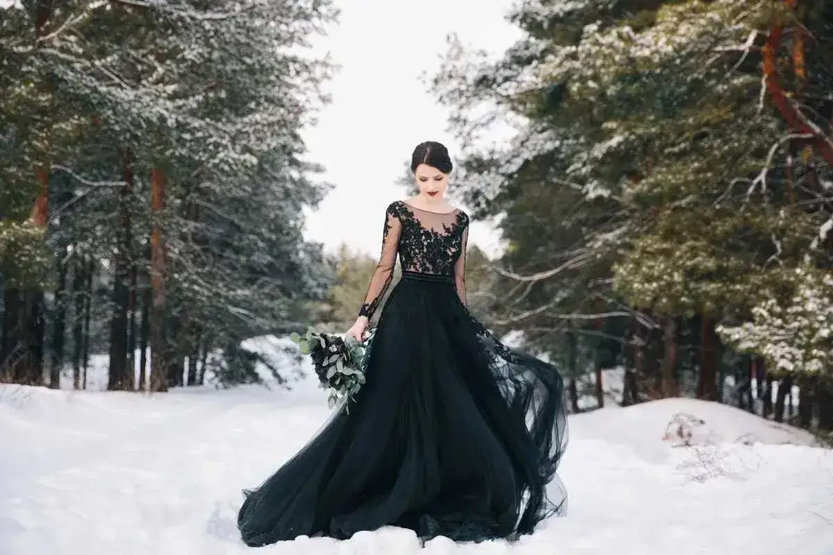 Una sposa in un bosco innevato indossa un abito da sposa nero. Il significato di un abito da sposa nero pu&ograve; variare, ma spesso rappresenta forza, mistero e individualit&agrave;.