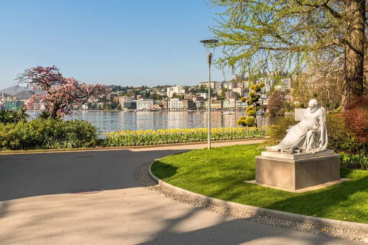 Statua nel parco sul lungolago di Lugano, con tulipani gialli e ciliegi in fiore. Perfetto per scoprire cosa vedere a Lugano in un giorno.