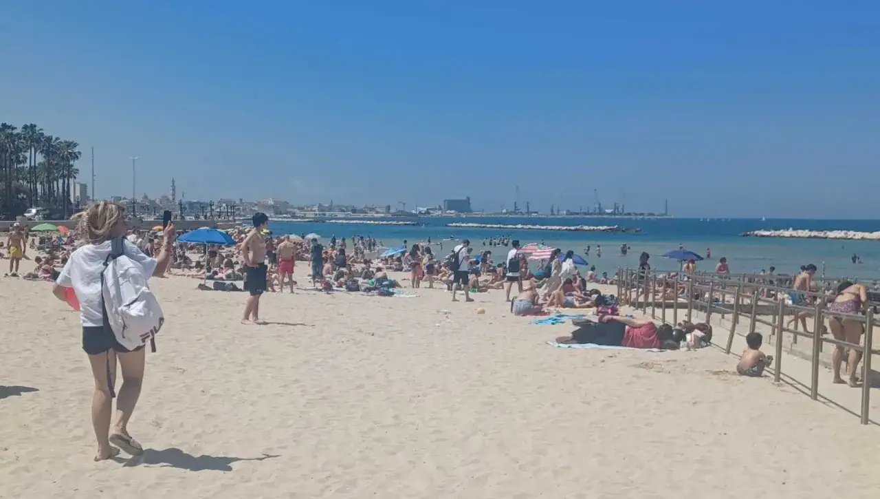 Spiaggia affollata a Bari, ideale per scoprire cosa vedere a Bari in 3 giorni. Gente al sole, mare azzurro e palme sullo sfondo.