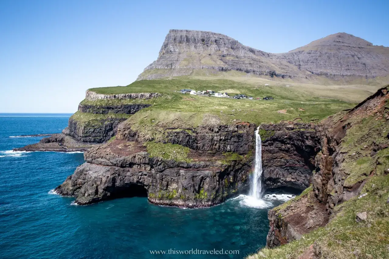 Cascata che si getta nell'oceano, con scogliere verdi e un villaggio in lontananza. Un vero spettacolo far oer.