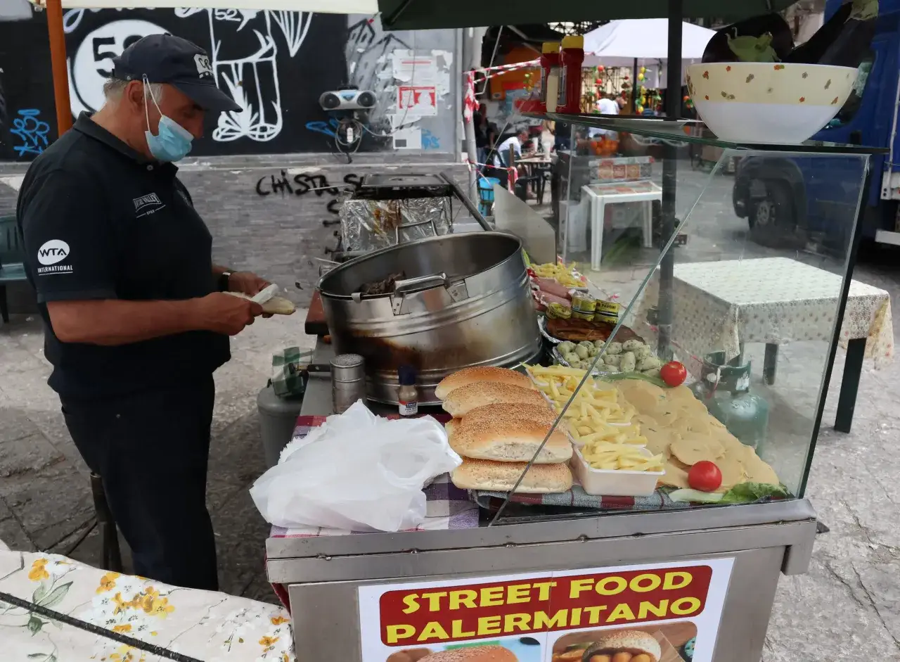 Venditore di street food palermitano prepara panini con patatine, formaggio e pomodoro. Cosa mangiare a Palermo? Qui trovi il meglio!