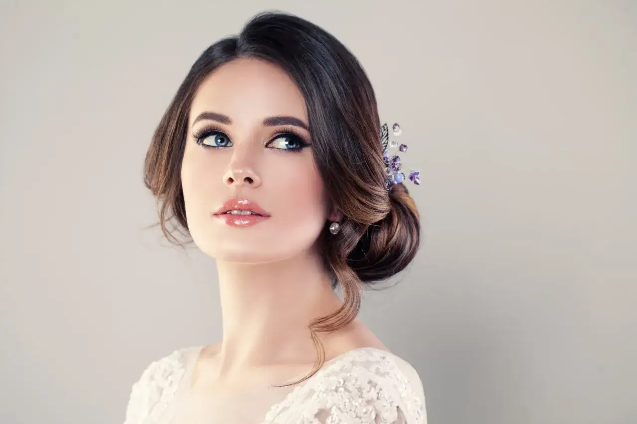 Splendido trucco da sposa semplice con labbra luminose e occhi intensi, acconciatura raccolta con accessori viola.