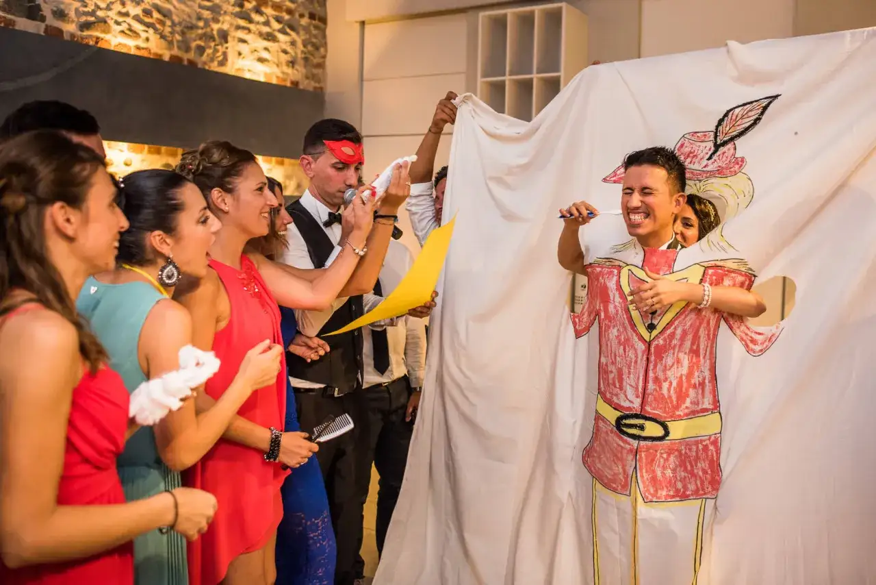 Un gruppo di persone partecipa a un divertente sposa gioco, con un uomo che finge di lavarsi i denti dietro un telo dipinto.