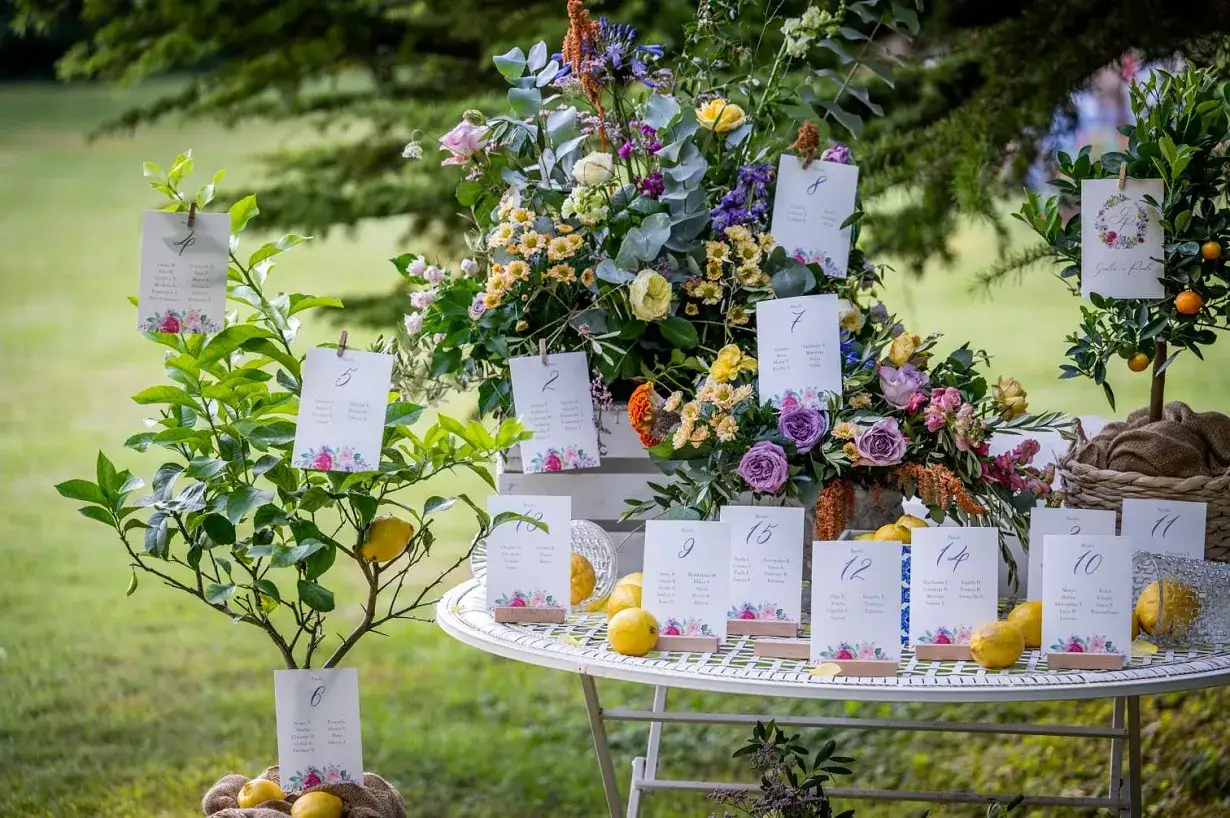 Tableau mariage idee: un tavolo bianco con fiori colorati, limoni e segnaposto numerati, perfetto per un matrimonio all'aperto.