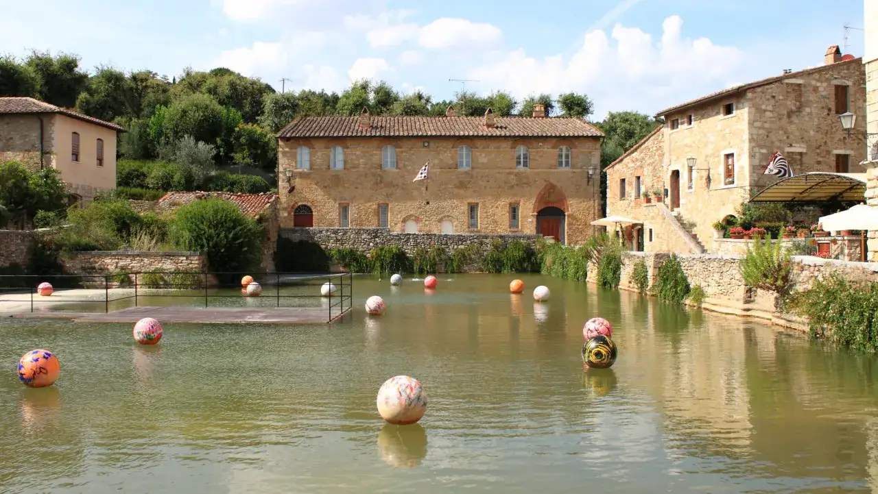 Un laghetto con sfere colorate galleggianti, circondato da antichi edifici in pietra. Un luogo incantevole tra i borghi da visitare in Piemonte.