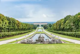 Giardini maestosi con fontane barocche e un palazzo imponente in lontananza, ricordano i fasti dei mulini reali.