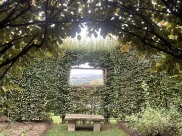 Un angolo verde incantevole, con un sedile in pietra che invita alla contemplazione del paesaggio visibile attraverso un'apertura nella siepe, come una finestra sul **palazzo di Cuzzano**.