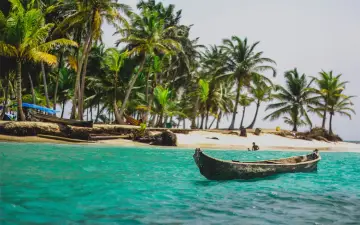 Barca in un mare turchese, palme e spiaggia. Un'idea perfetta per sapere dove andare al mare a Capodanno.