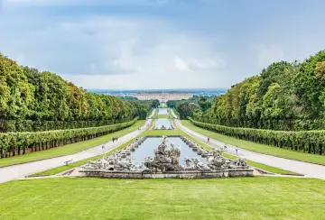 Giardini maestosi con fontane barocche e un palazzo imponente in lontananza, ricordano i fasti dei mulini reali.