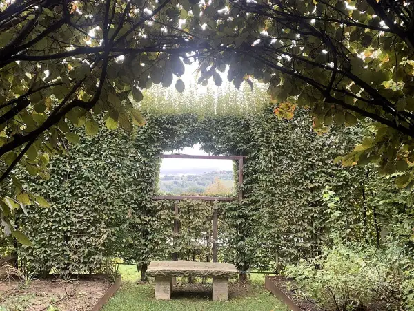 Un angolo verde incantevole, con un sedile in pietra che invita alla contemplazione del paesaggio visibile attraverso un'apertura nella siepe, come una finestra sul **palazzo di Cuzzano**.