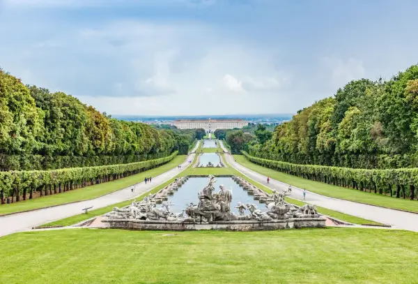 Giardini maestosi con fontane barocche e un palazzo imponente in lontananza, ricordano i fasti dei mulini reali.