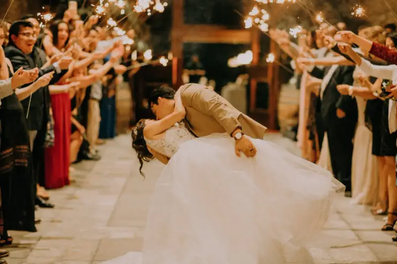 La sposa e lo sposo si baciano tra le scintille dei bengala, circondati da amici e parenti festanti. Un momento magico che sembra uscito da un gioco.