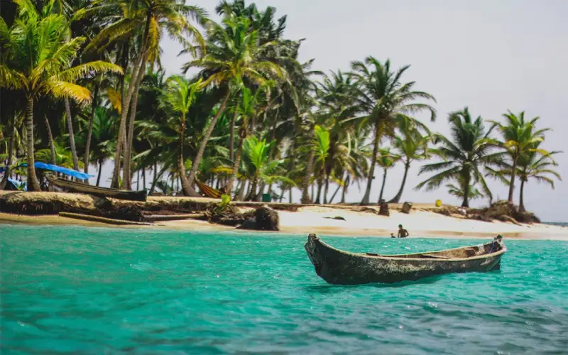 Barca in un mare turchese, palme e spiaggia. Un'idea perfetta per sapere dove andare al mare a Capodanno.