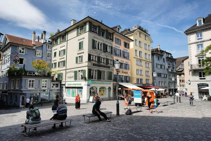 Piazza di Zurigo con edifici colorati, negozi e persone che passeggiano. Ideale per scoprire cosa vedere a Zurigo in un giorno.