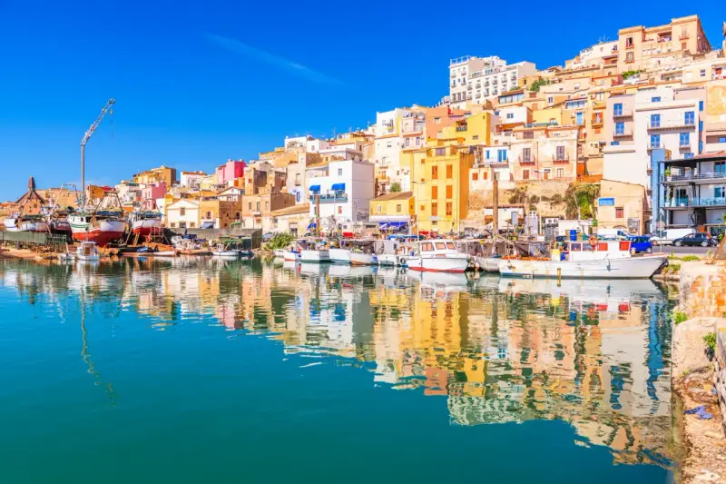 Porto di Sciacca, cosa vedere: barche da pesca ormeggiate e case colorate che si specchiano sull'acqua cristallina.
