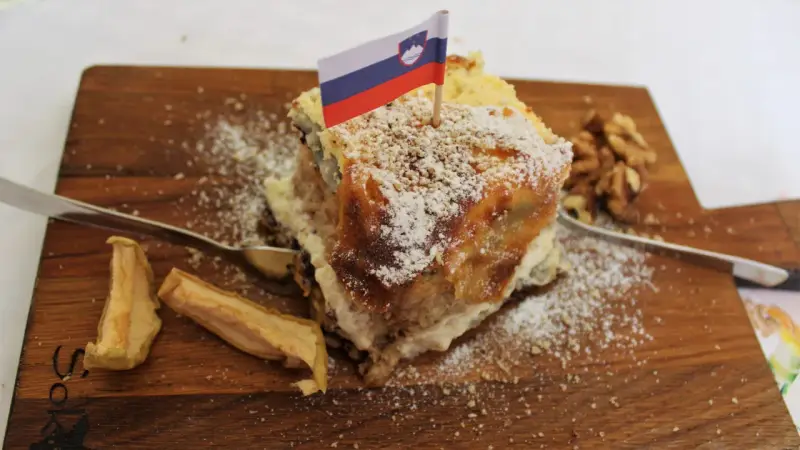 Una fetta di torta con bandierina slovena, noci e mele essiccate, un assaggio dei piatti tipici sloveni.